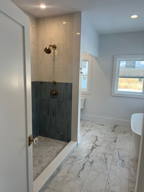 Bathroom with walk-in shower. Gray marble floor, white walls. Shower features gray and blue tile, gold fixtures.
