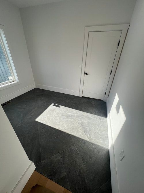 Small room with dark tiled floor, white walls, a closed door, and window. Sunlight illuminates the floor.