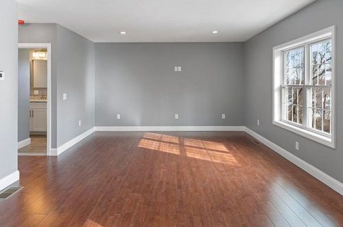 Empty room with gray walls, hardwood floor, and window letting in sunlight.