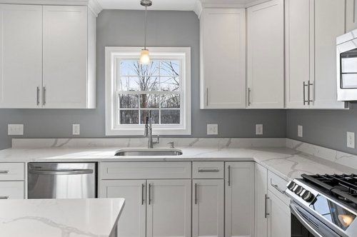 White kitchen with marble countertops, cabinets, stainless steel appliances, and a window.