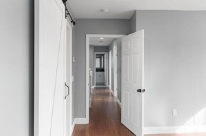 Hallway with gray walls, white doors, and wood flooring. A barn door is on the left.