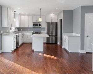 Modern kitchen with white cabinets, stainless steel appliances, and wood flooring. Gray walls and a small island are also featured.