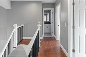 Hallway with gray walls, wood floor, white doors and trim, black and white banister, and bathroom doorway.