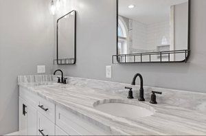 Bathroom with white cabinets, marble countertop, black fixtures, and two mirrors.