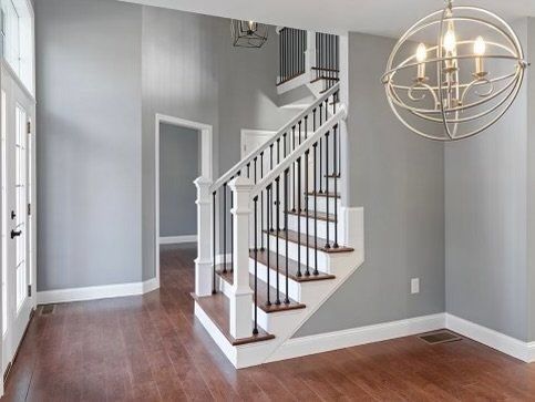 Interior view of a house with a staircase, gray walls, wood floors, and a decorative light fixture.