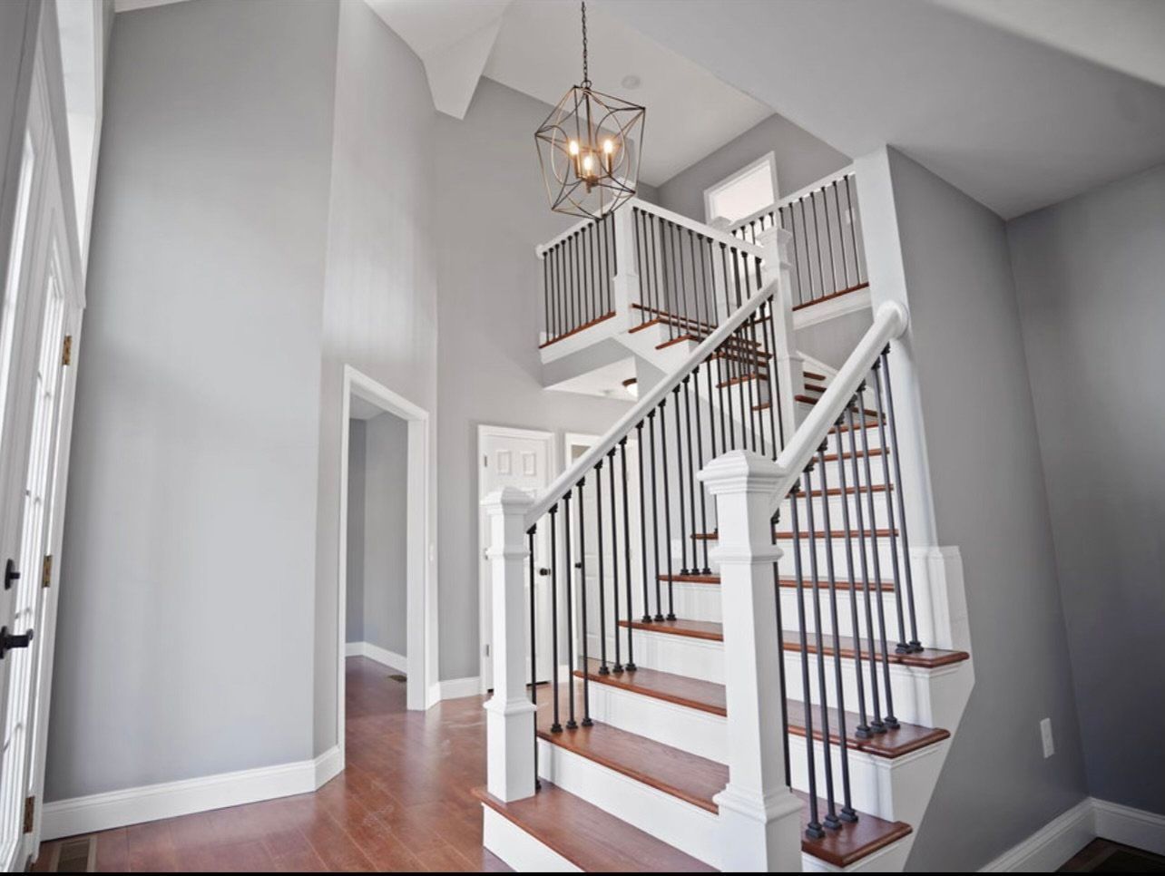 Staircase with wooden steps, white railing, and grey walls. A chandelier hangs from the high ceiling.