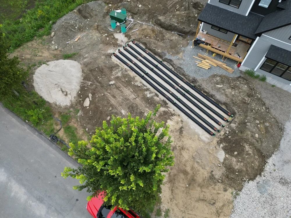 Construction site with buried pipes, dirt, a house, and a red car.