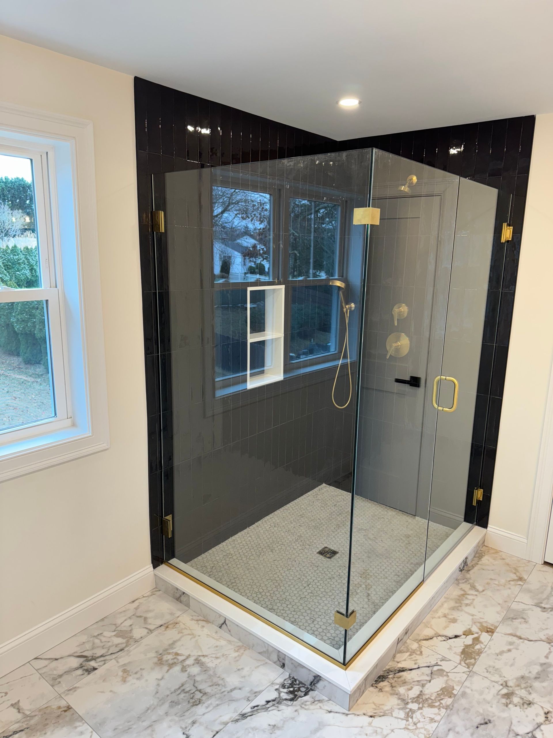 Corner shower with gray tile, glass door, and gold fixtures.