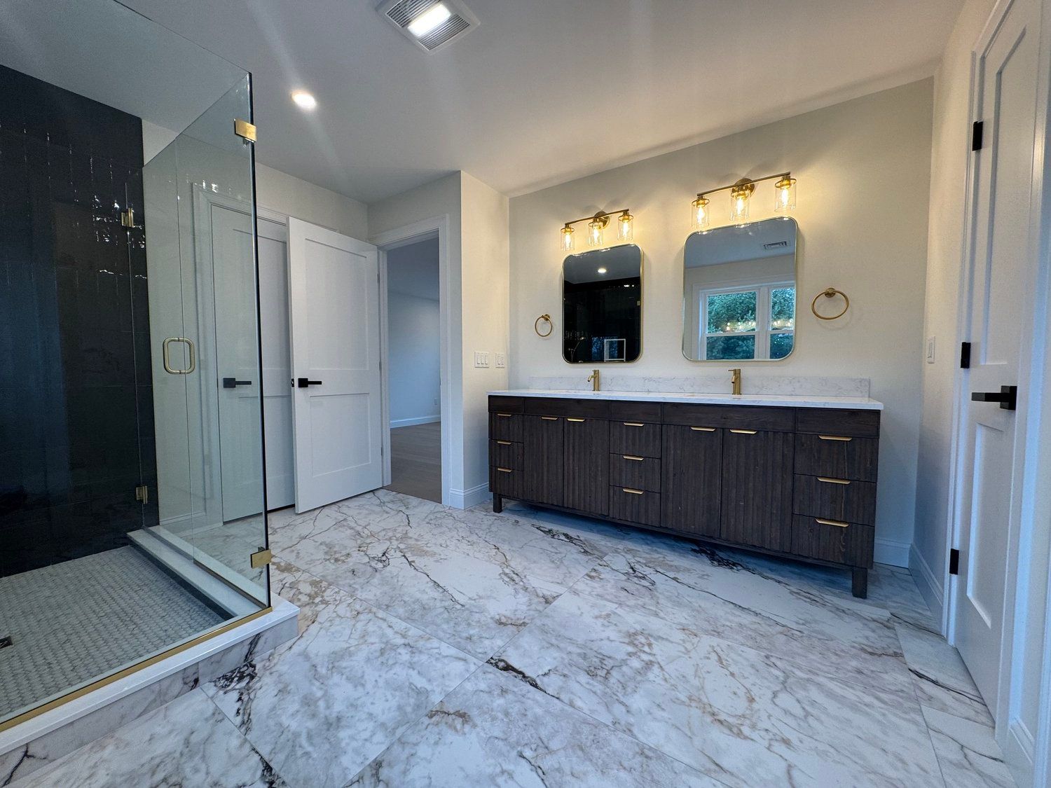 Bathroom with marble floors, dark wood vanity, glass shower, and gold fixtures.