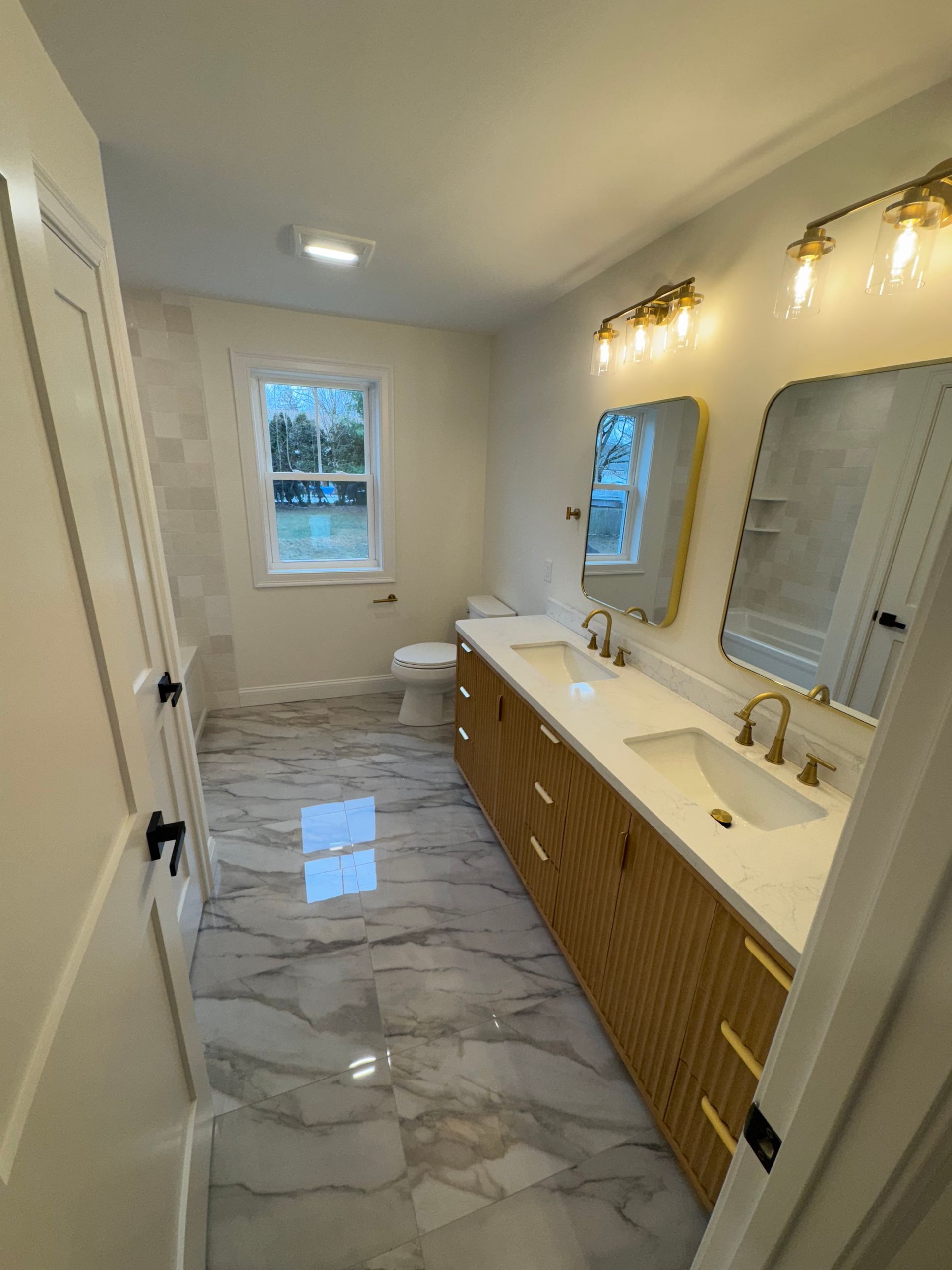 Bathroom with marble floors, double vanity, gold fixtures, and a window.