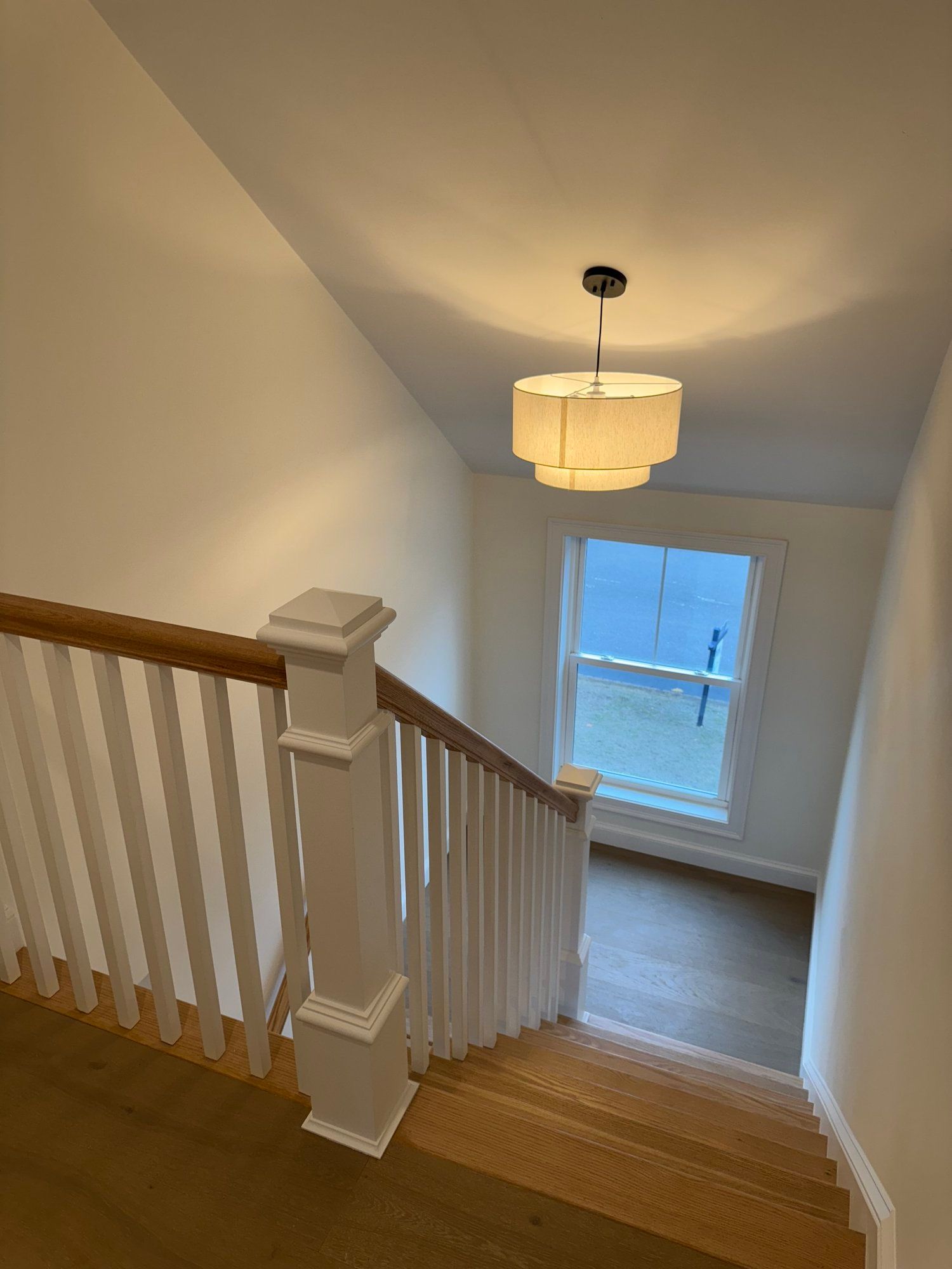 Staircase with white railing and wood steps, leading down to a window. A light fixture hangs from the ceiling.