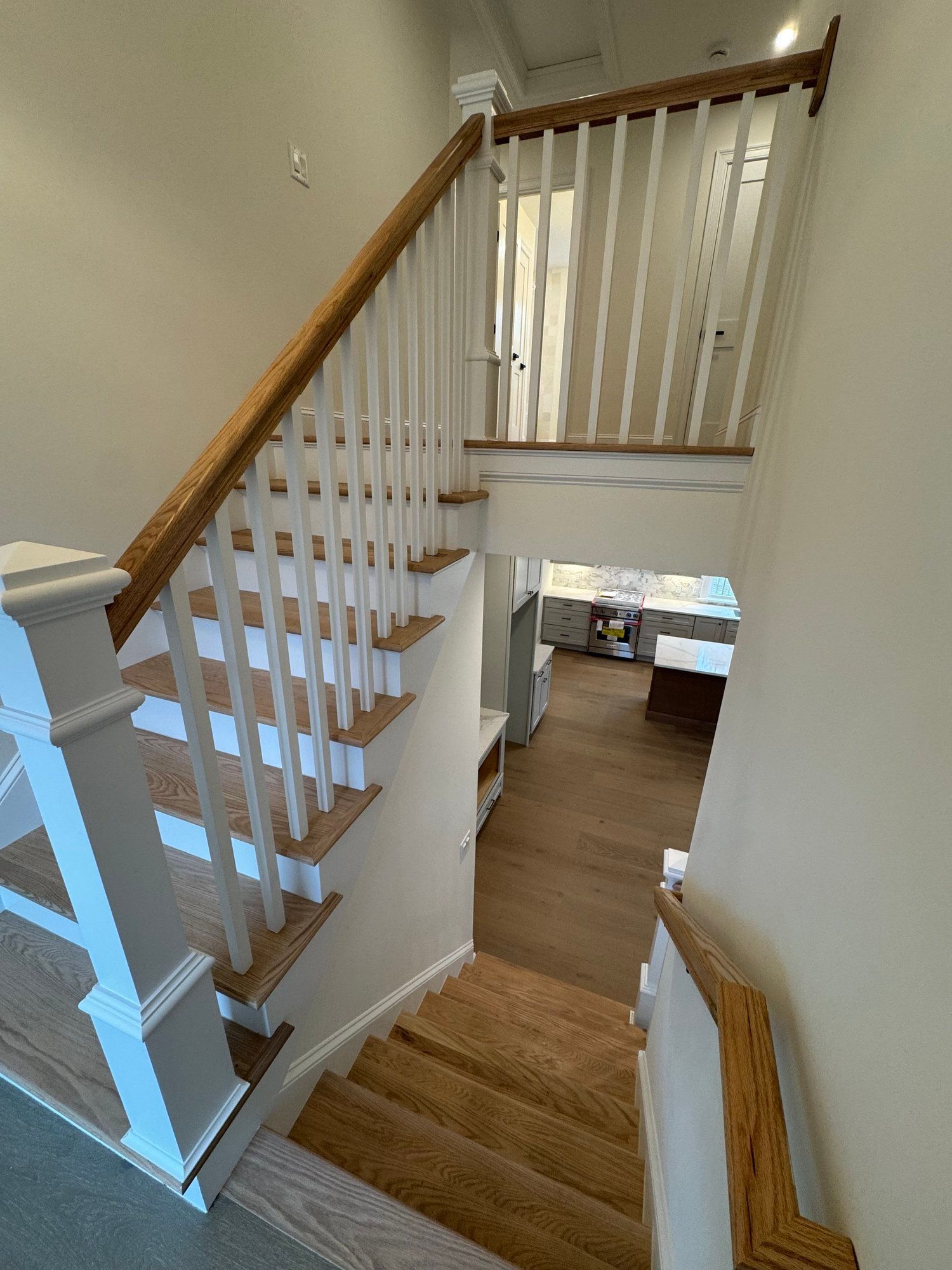 Wooden staircase with white banister leading down to a kitchen.