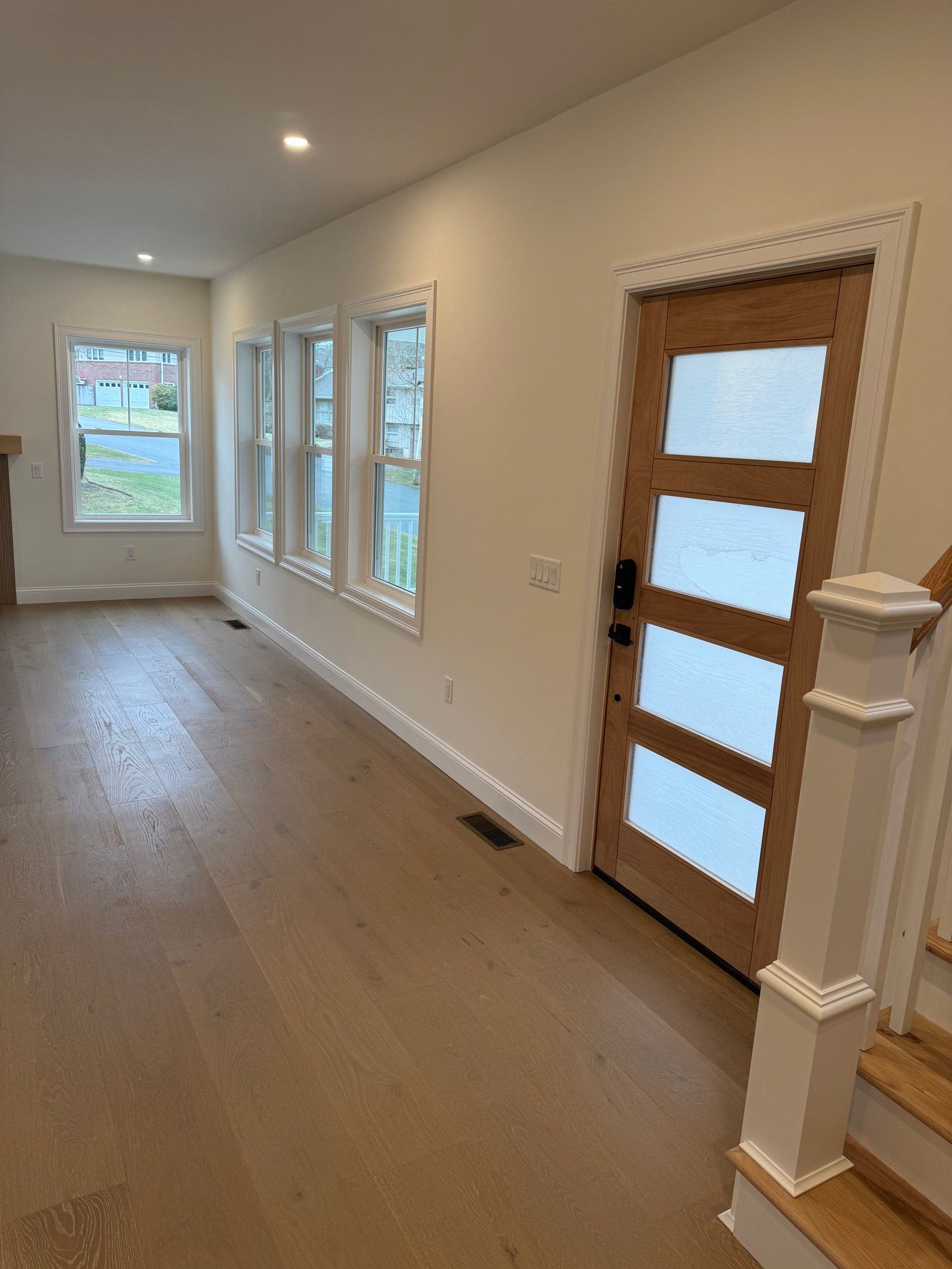 Interior view of a house with wooden floors, cream walls, and a light wooden door with glass panels.