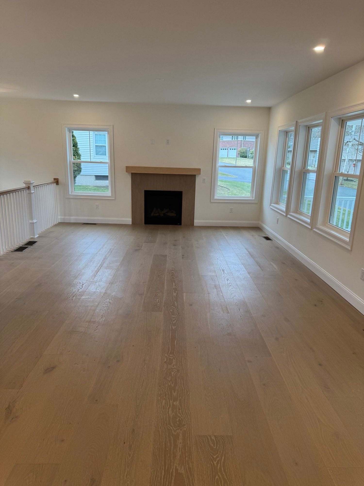 Empty room with wooden floor, fireplace, and windows.
