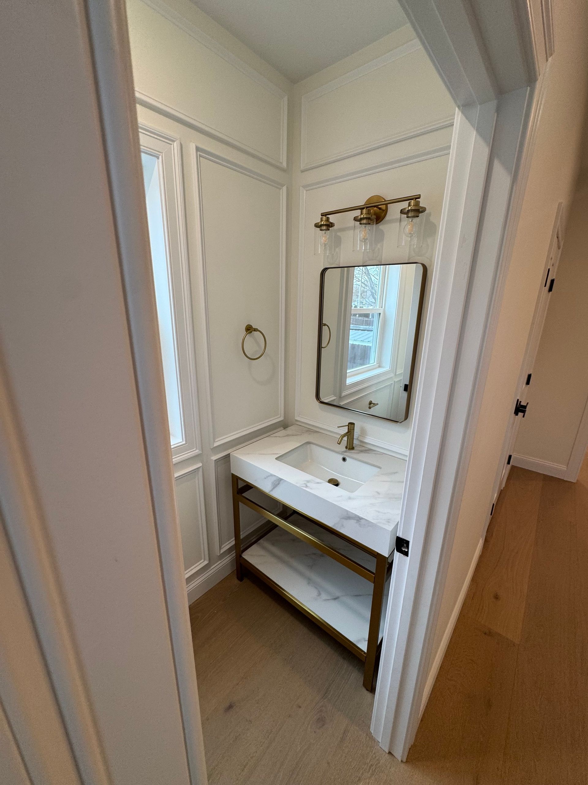 Small, ornate powder room with marble vanity, gold fixtures, and a window.