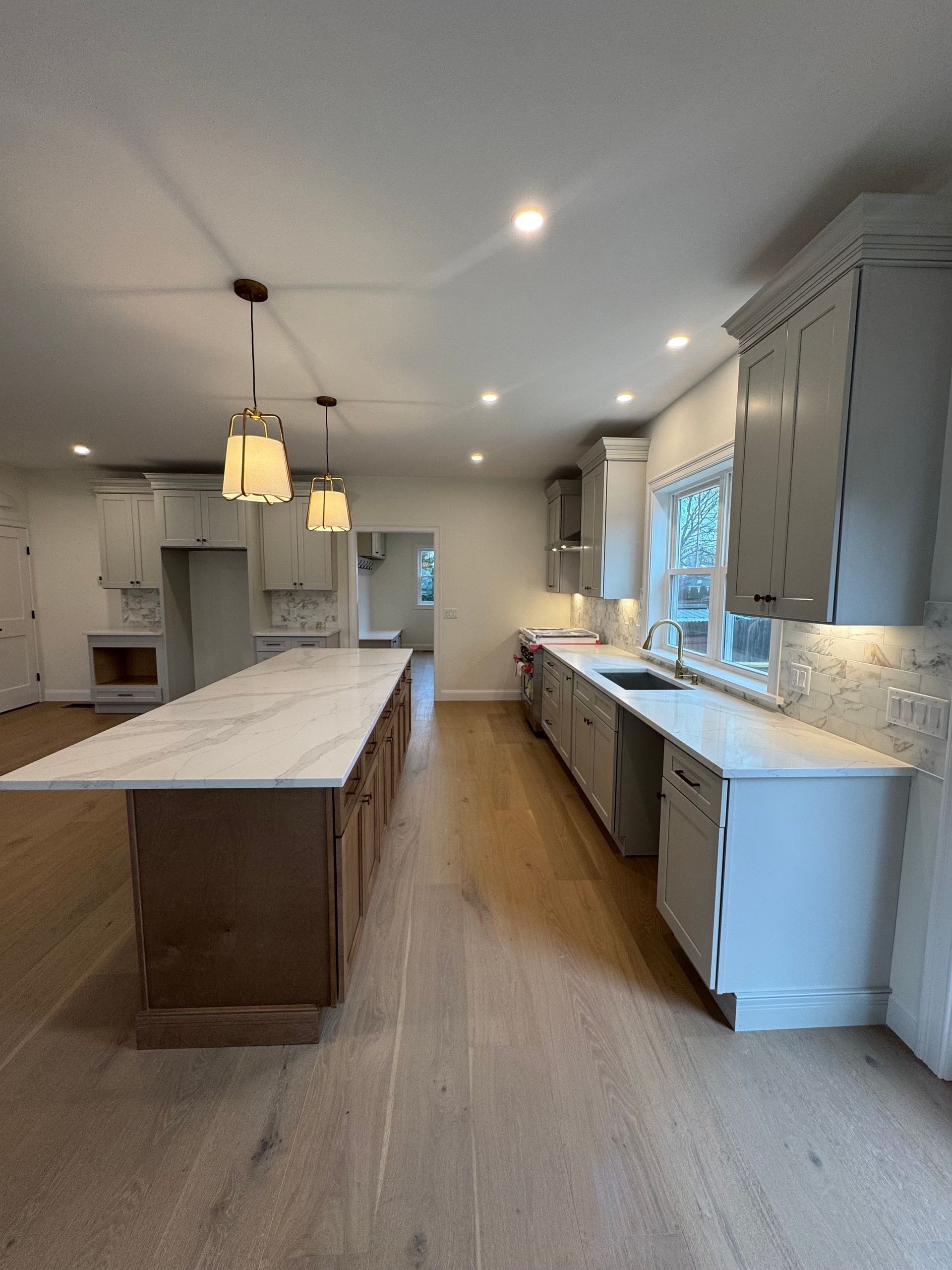 Newly renovated kitchen with a long island, light wood floors, and white and gray cabinets.