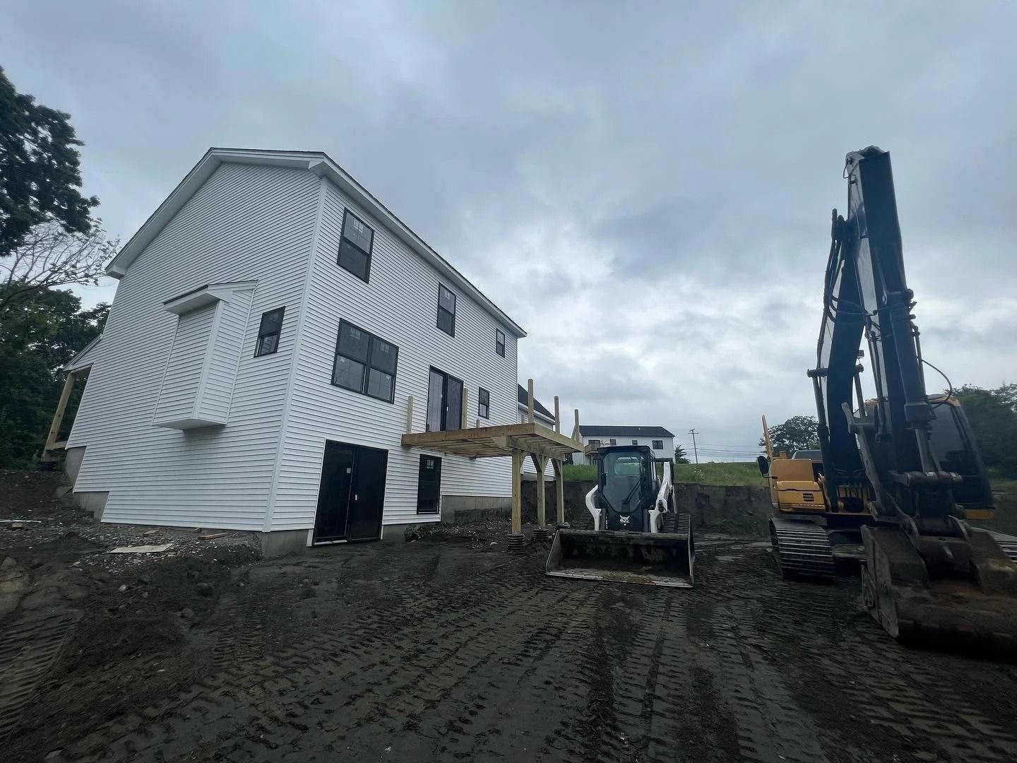 Construction site: white house with siding, heavy machinery, cloudy sky.