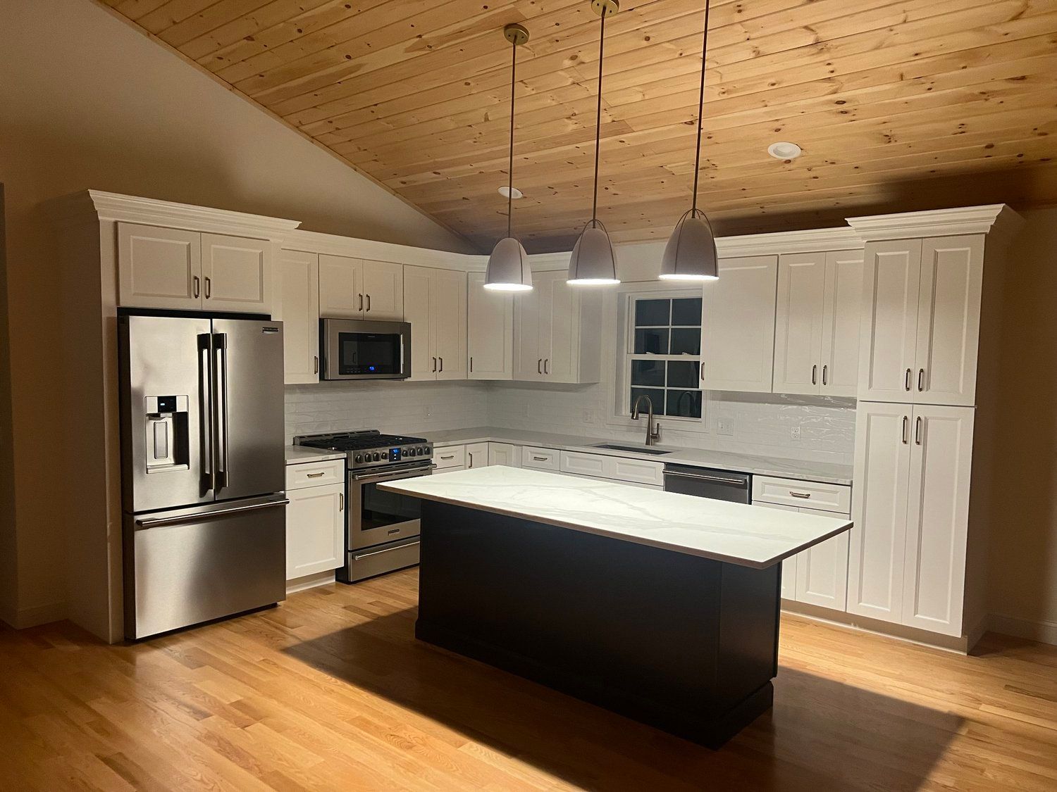 Modern kitchen with white cabinets, stainless steel appliances, and dark island. Wood ceiling and floor.