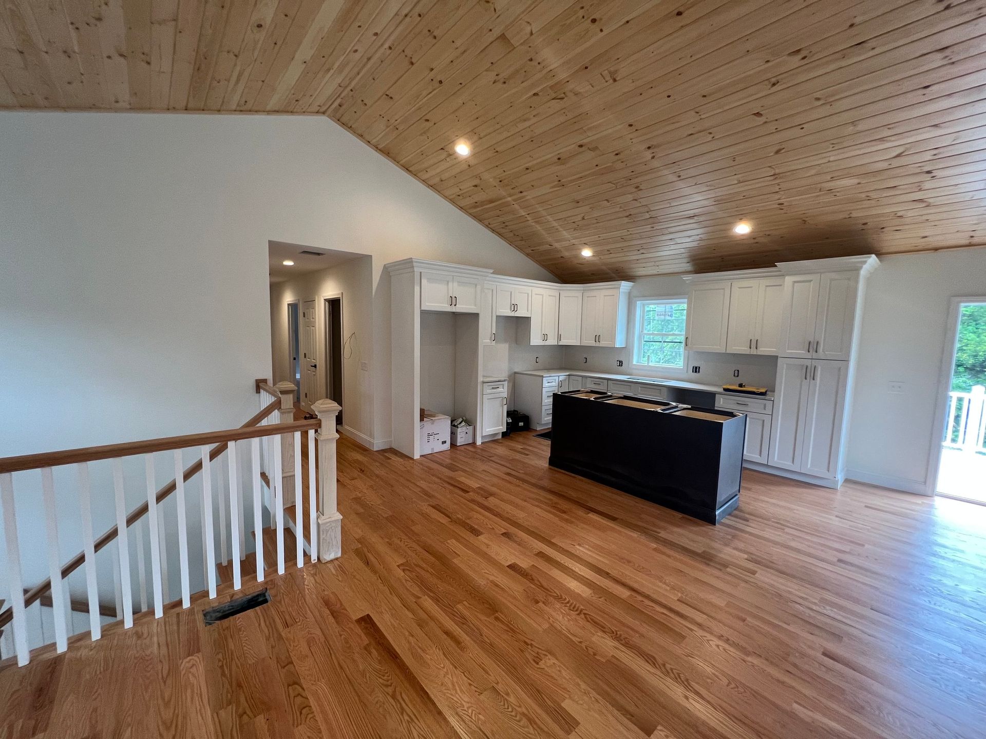 Open kitchen with white cabinets, wood floors, and wooden ceiling.