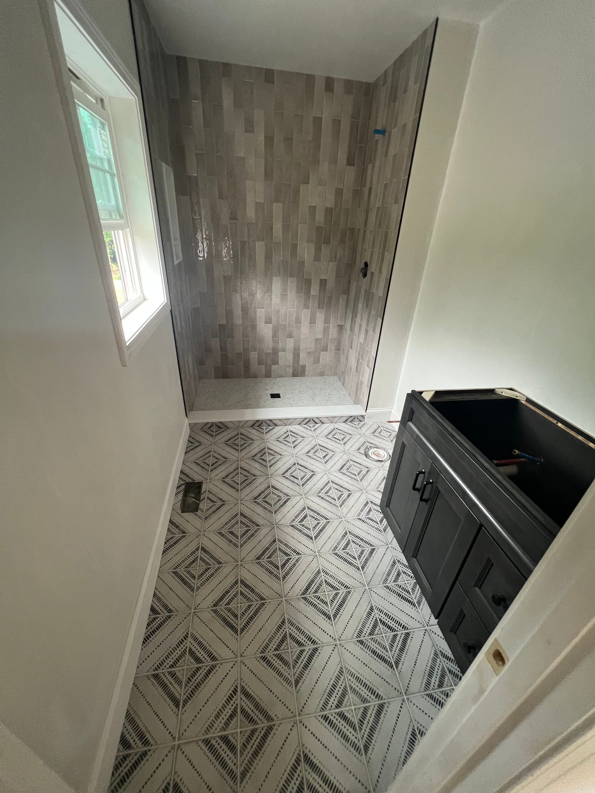 Bathroom with patterned floor tiles, gray shower, black vanity, and window.