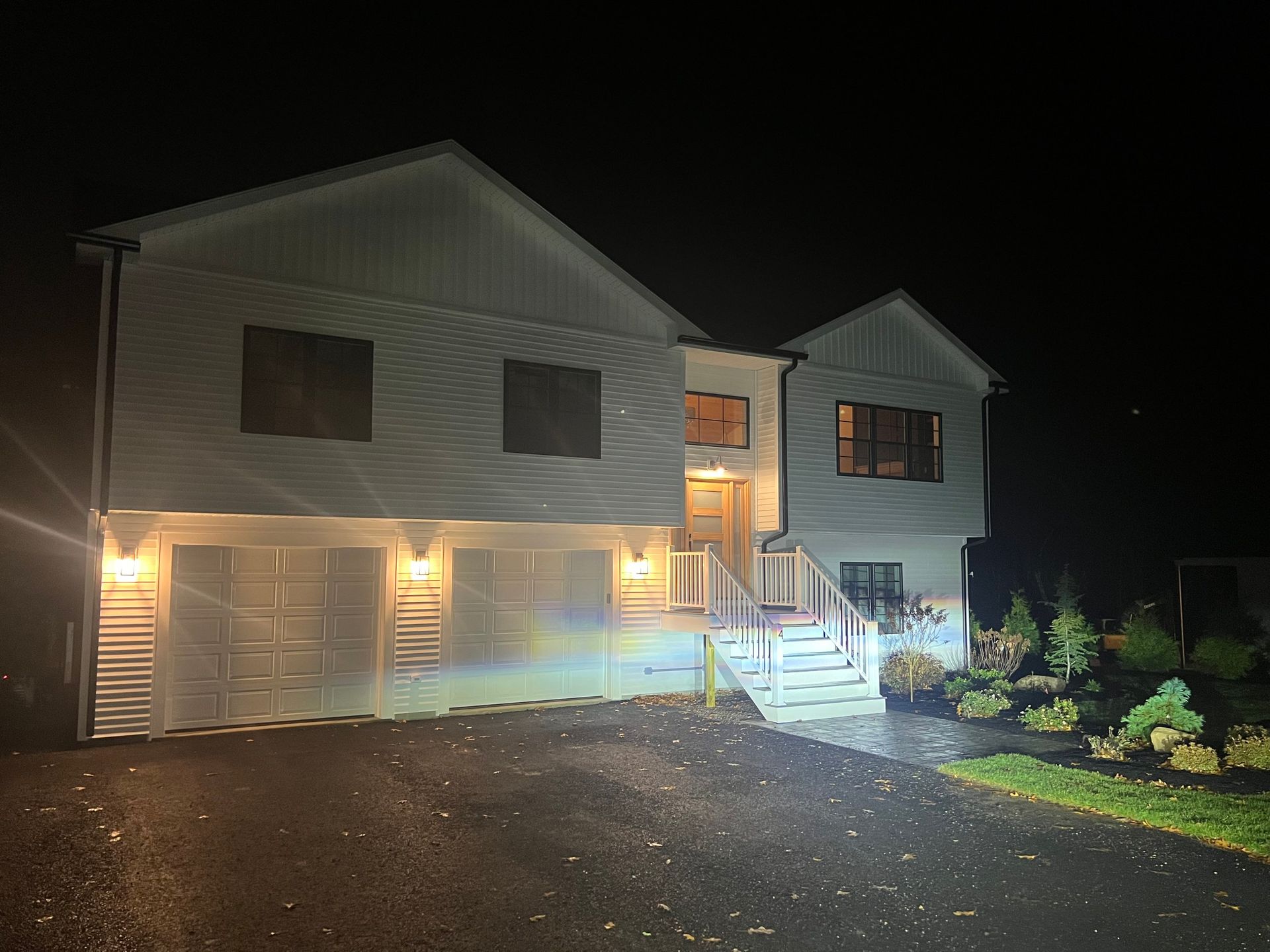 Two-story white house at night with garage, lit steps, and driveway.