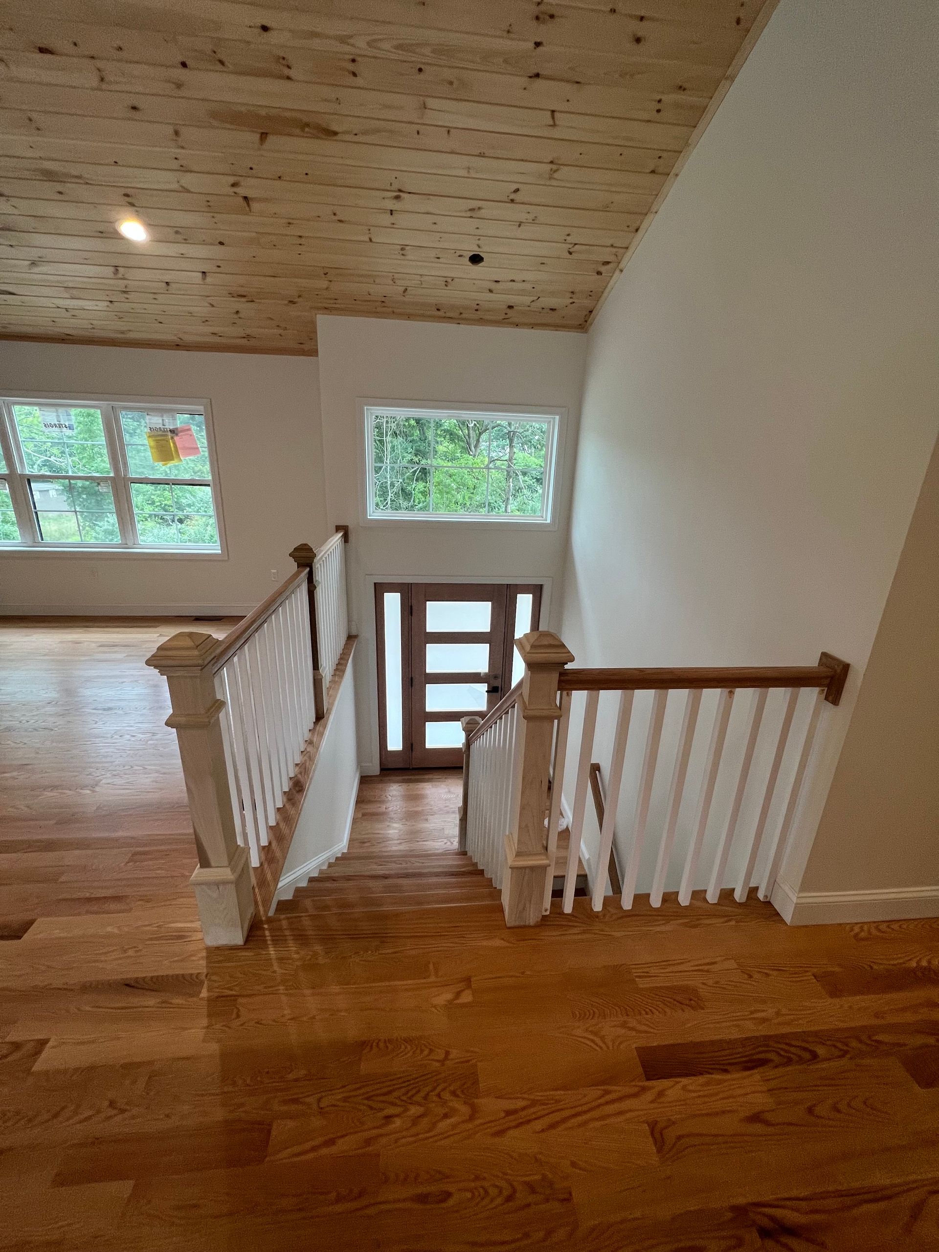 Wooden staircase leading down to a doorway with windows; wood floor and ceiling; white walls.