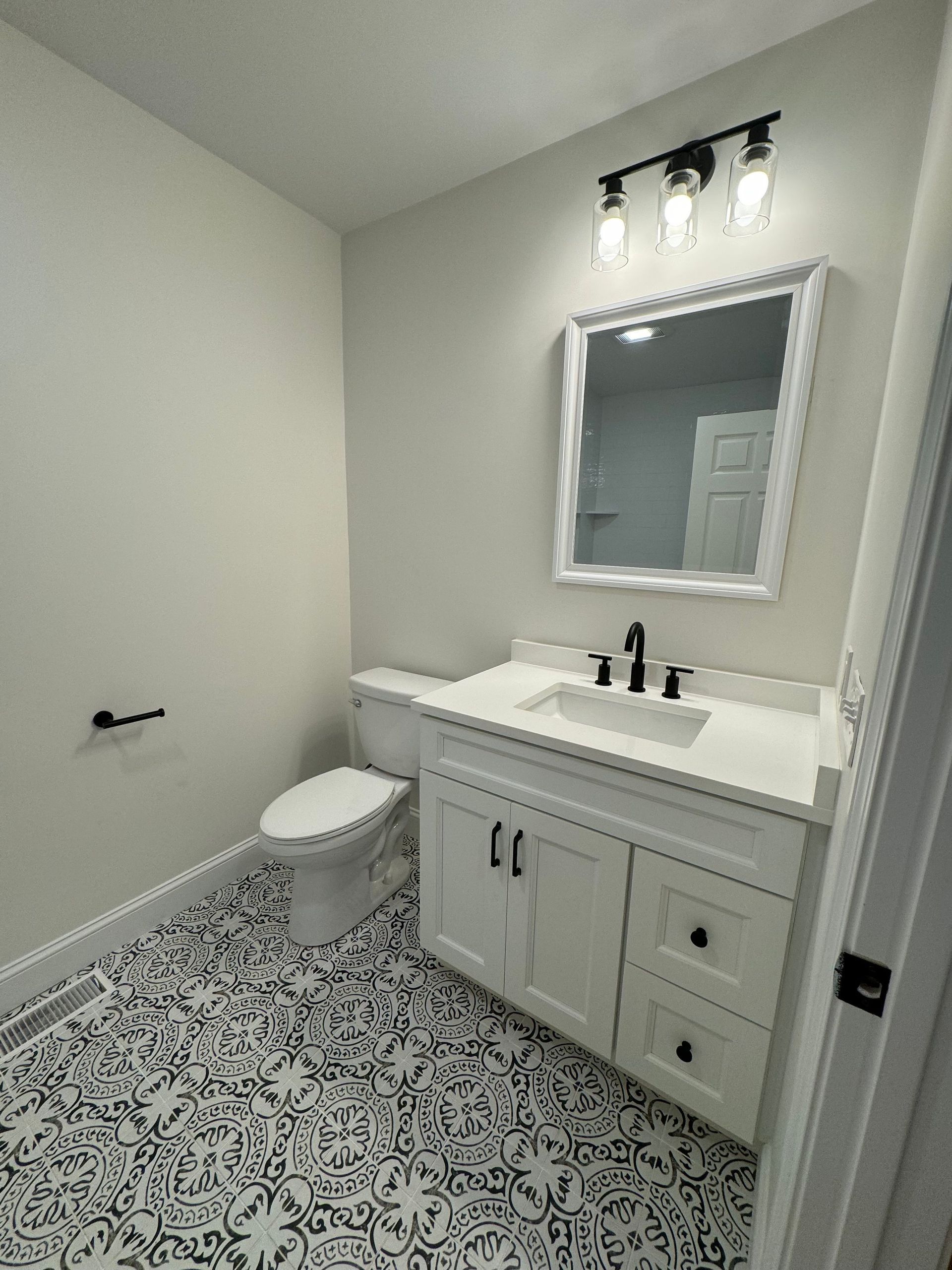A newly renovated bathroom with white walls, black and white patterned floor, and white vanity.