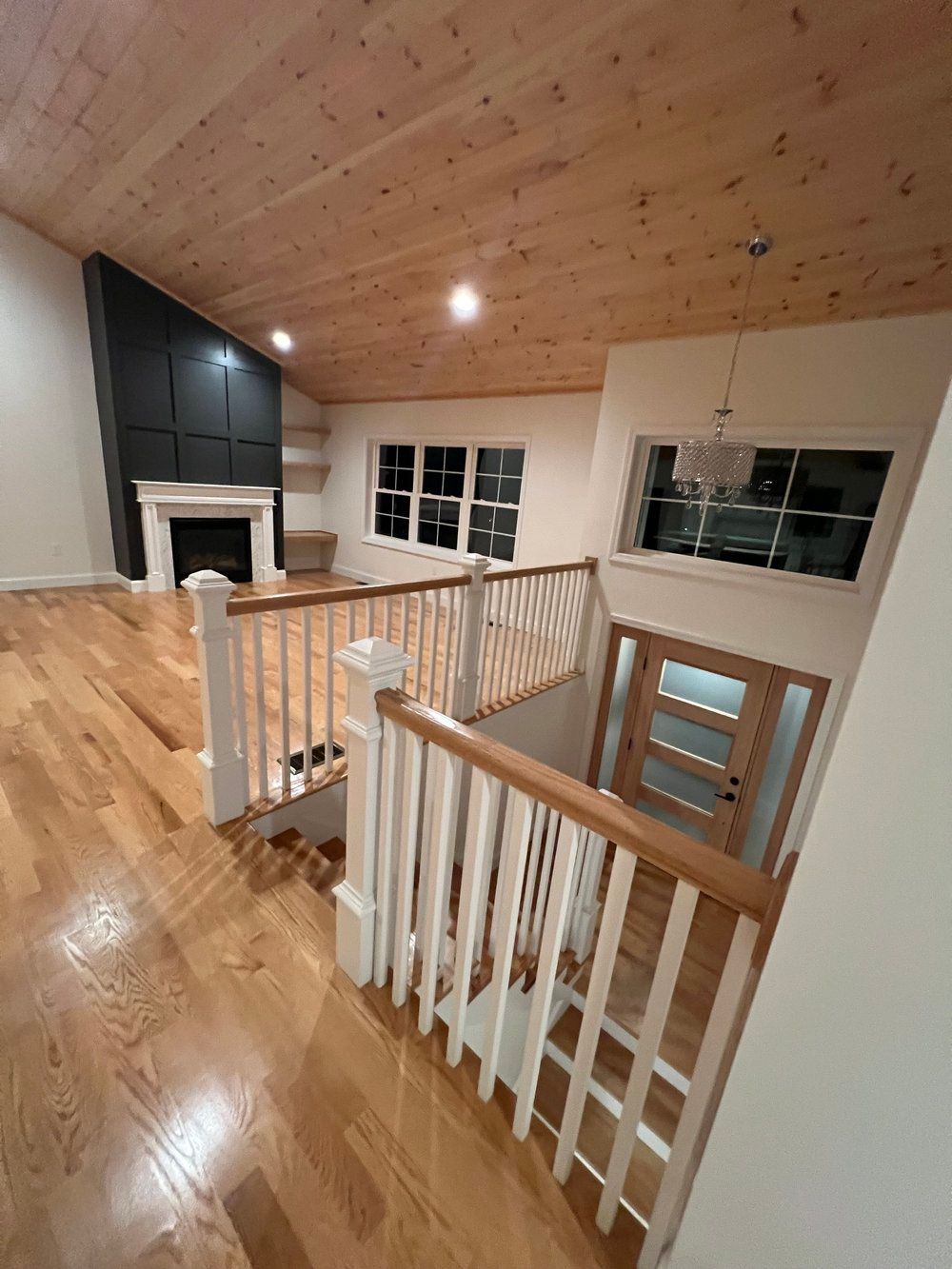 Interior view of a house: hardwood floors, wooden ceiling, white railing, fireplace, and staircase.