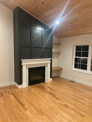 A modern living room with a gray paneled wall above a fireplace, wooden floors, and a wood ceiling.