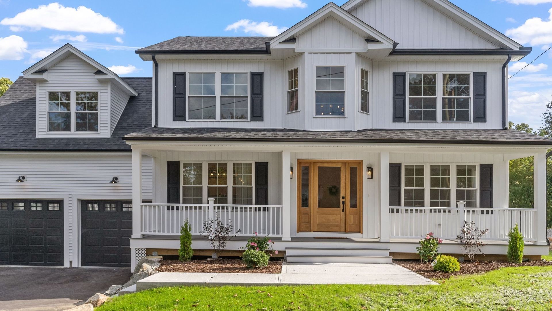 White two-story house with black shutters, a wooden door, and a front porch, set on a green lawn.