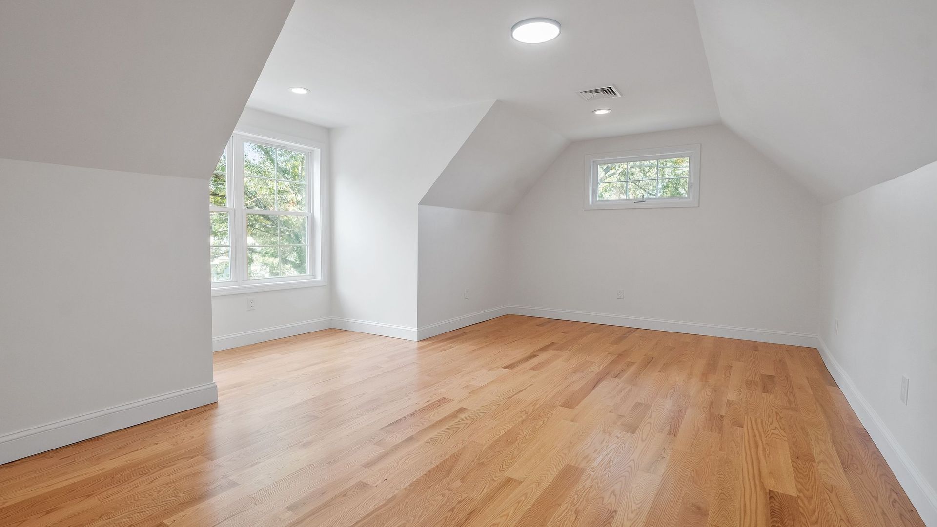 Empty room with hardwood floors, white walls, and two windows.