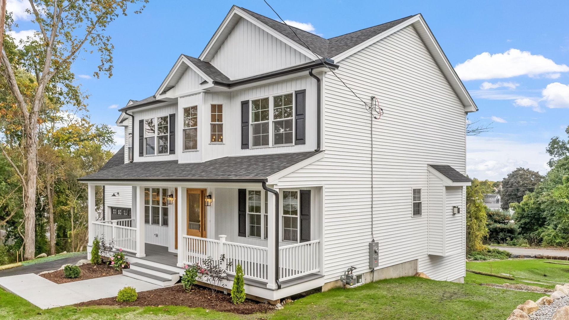 White two-story house with black shutters and trim, wooden front door, and a porch. Green lawn and trees.