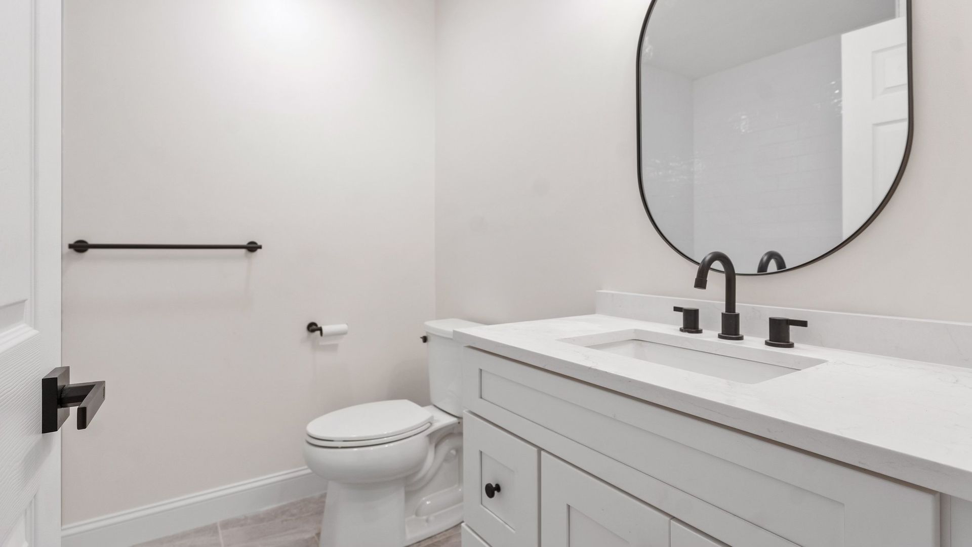White bathroom with a toilet, vanity, and black fixtures.