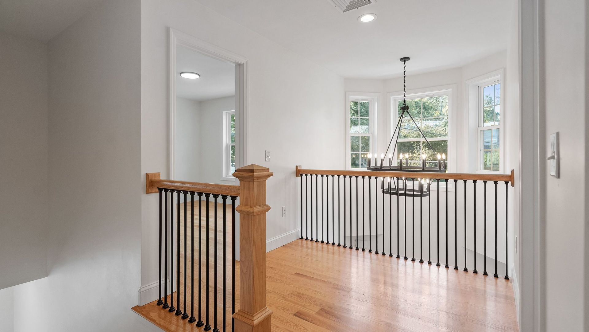 Interior view of a second-floor landing with wood floors, a black and wood railing, and a bay window.