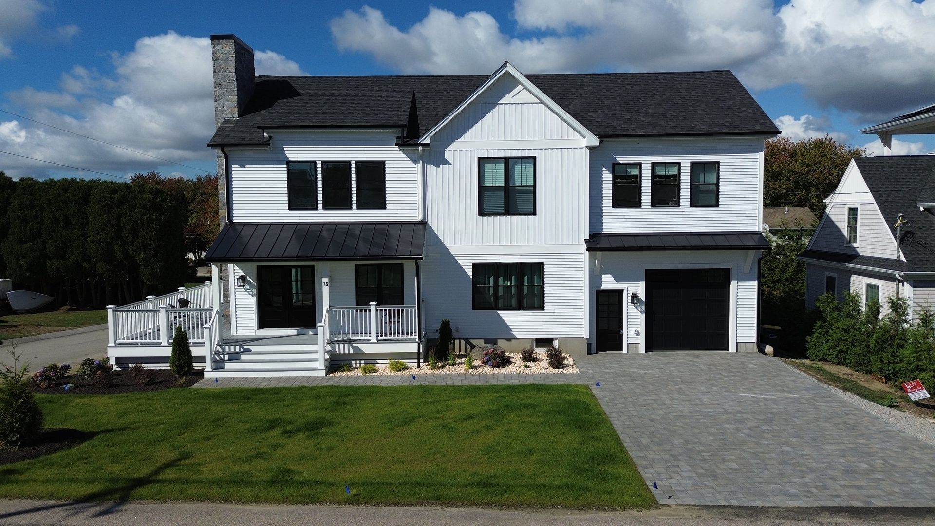 White two-story house with black trim, dark roof, and a gray driveway on a sunny day.