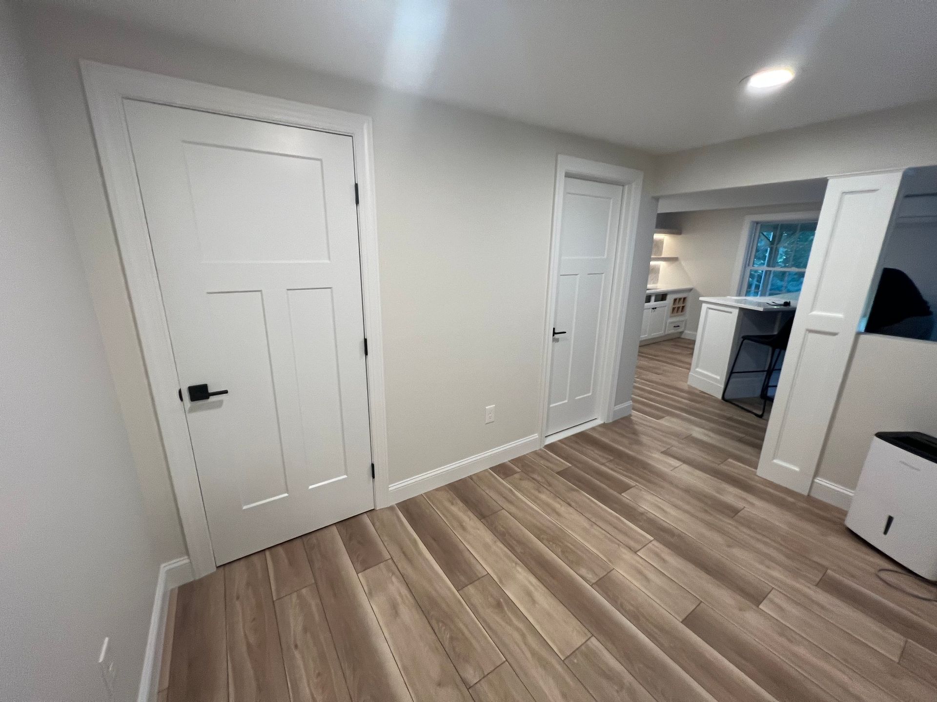 Interior view of a room with wood flooring, white doors, and a glimpse into another room with a counter and cabinets.