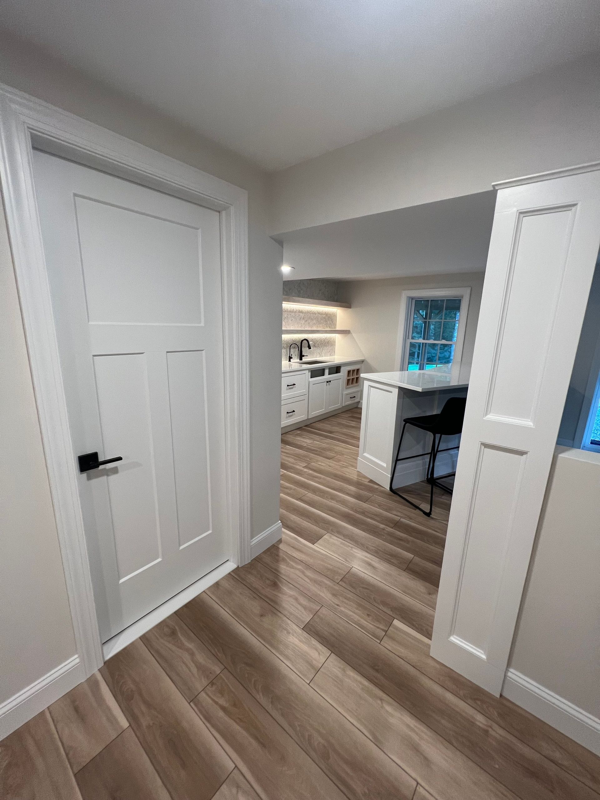 Interior view of a hallway leading to a kitchen with wood flooring and white walls.
