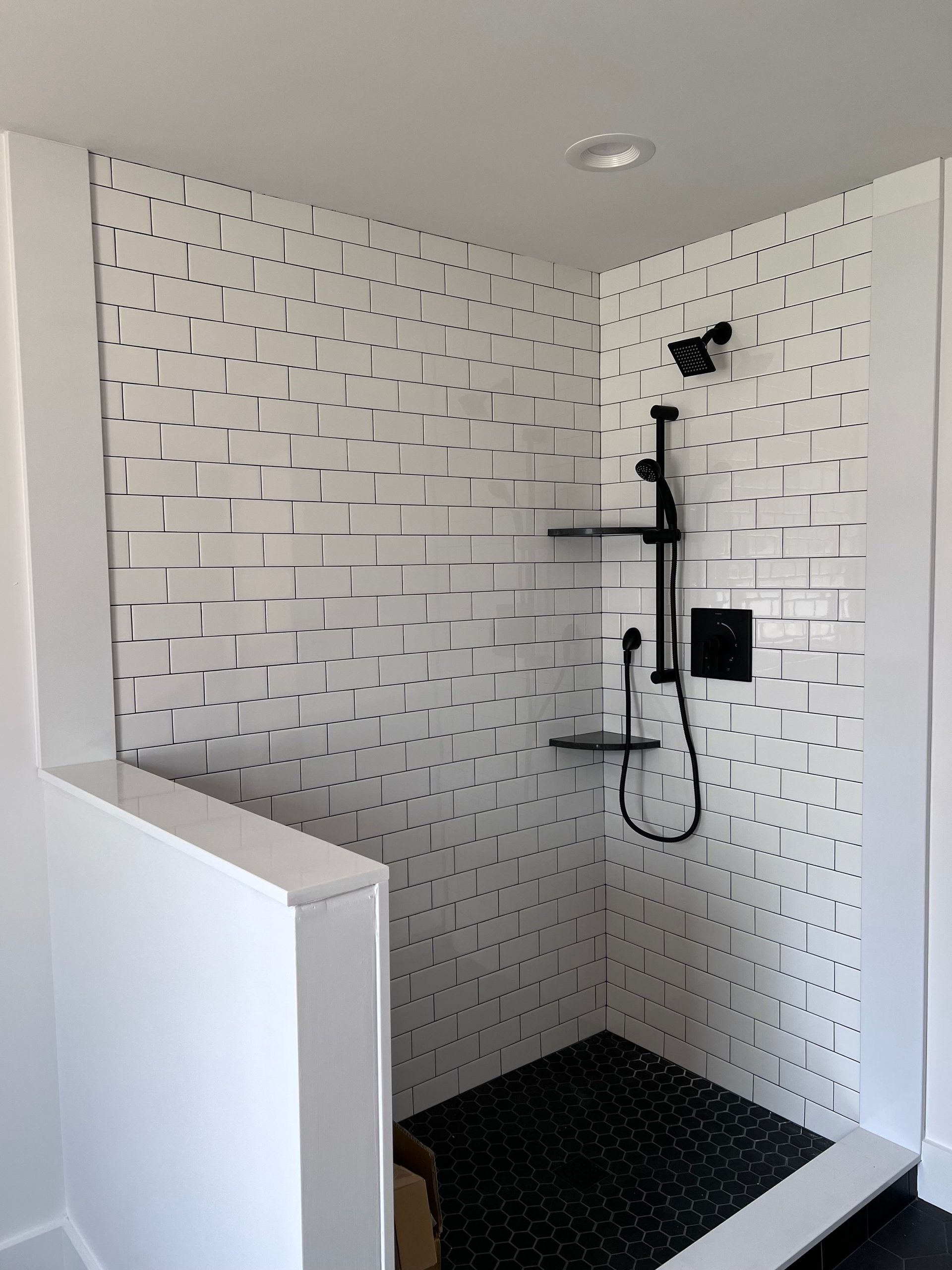 White tiled shower with black fixtures and dark floor.