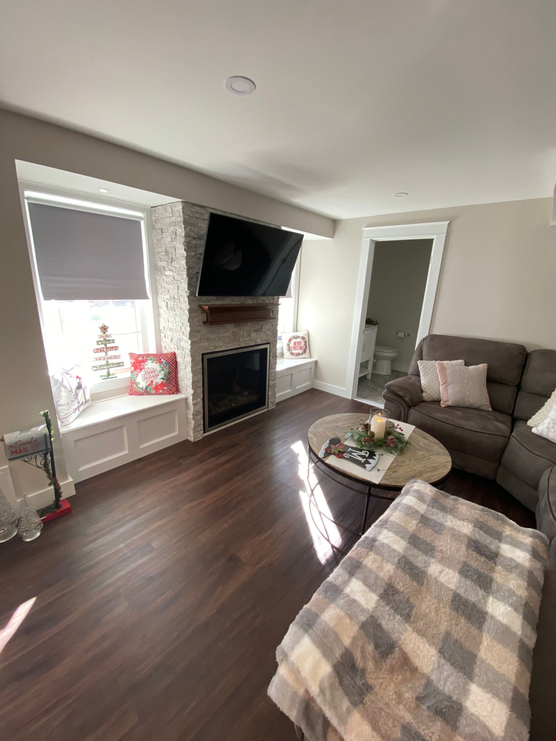 Living room with fireplace, TV, sectional sofa, and window seat. Dark wood flooring.