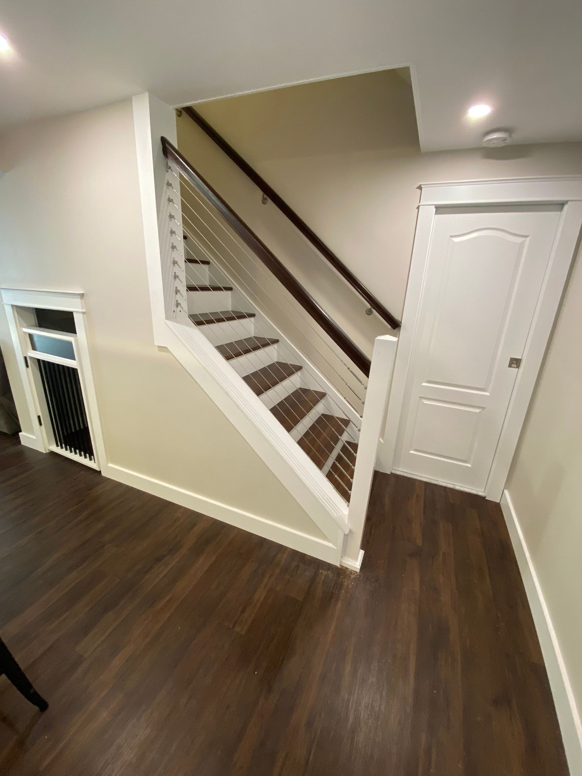 Staircase with white railing, wooden steps, and brown flooring. Beige walls with white trim and a white door.