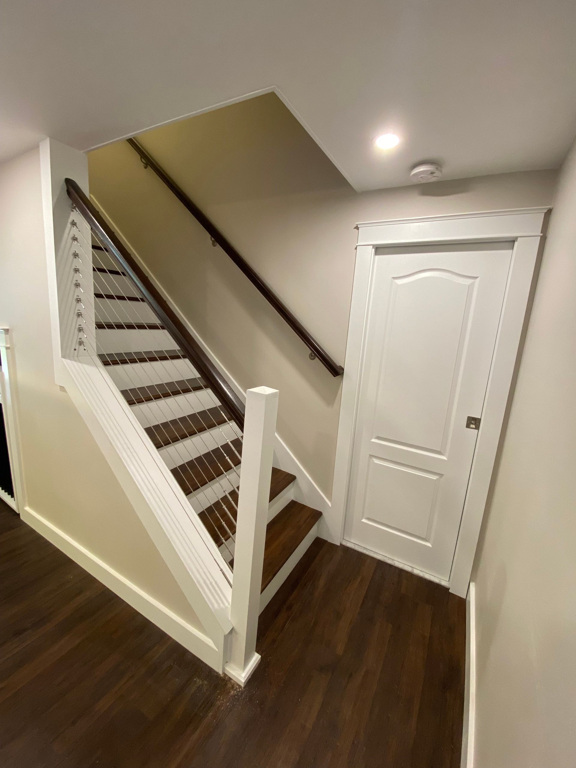 Staircase leading up with white risers, brown treads, a dark handrail, and a white door to the right.