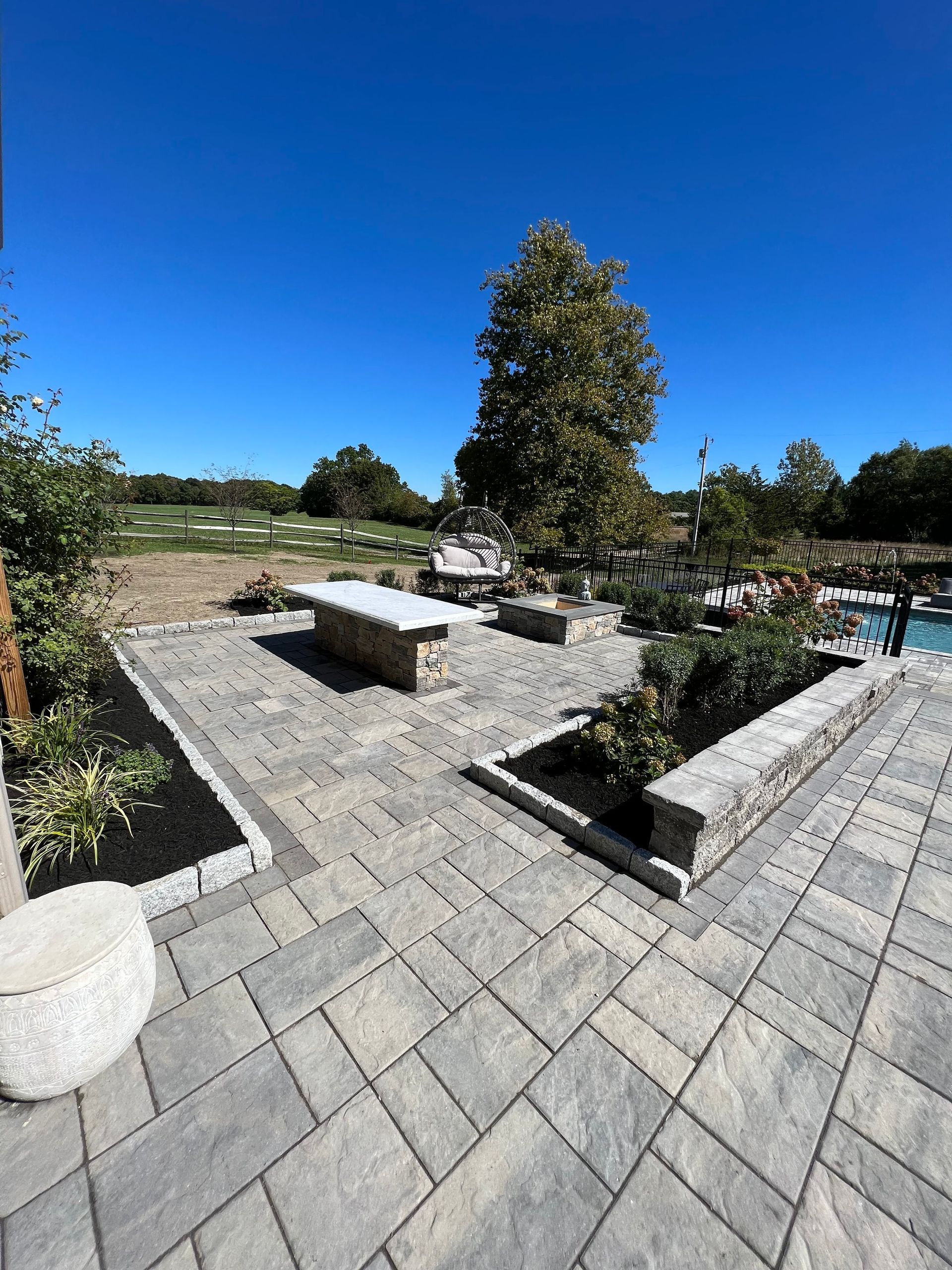 Patio with stone pavers, built-in planters, and a table under a clear blue sky.