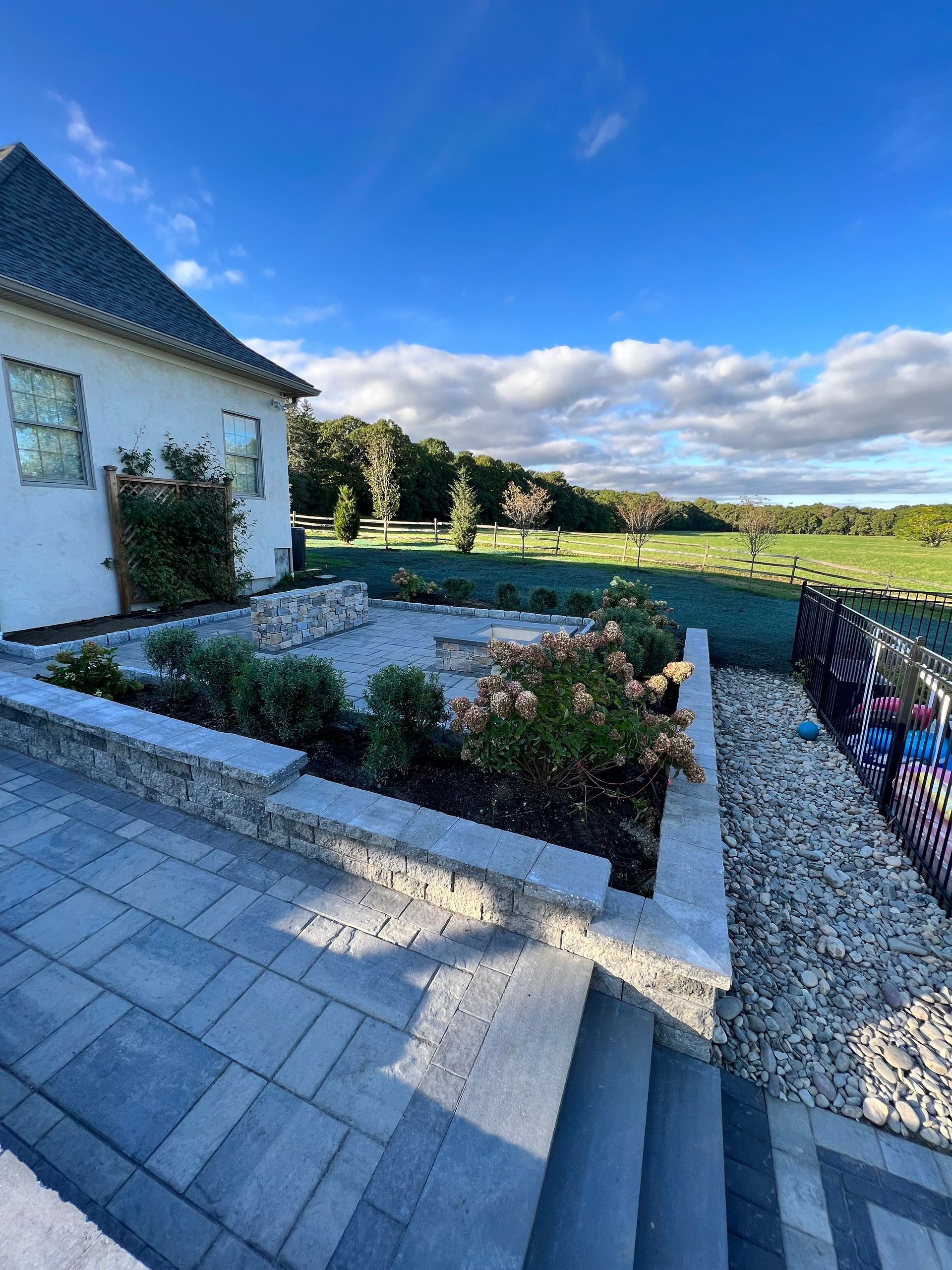 Stone patio with tiered wall, house, and green golf course under a blue sky.