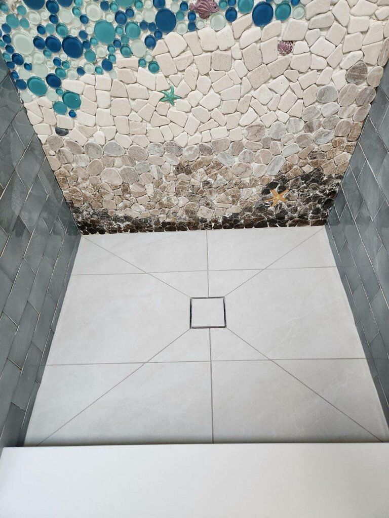 Shower with mosaic tile ceiling in shades of blue, beige, and white, and gray floor tiles.