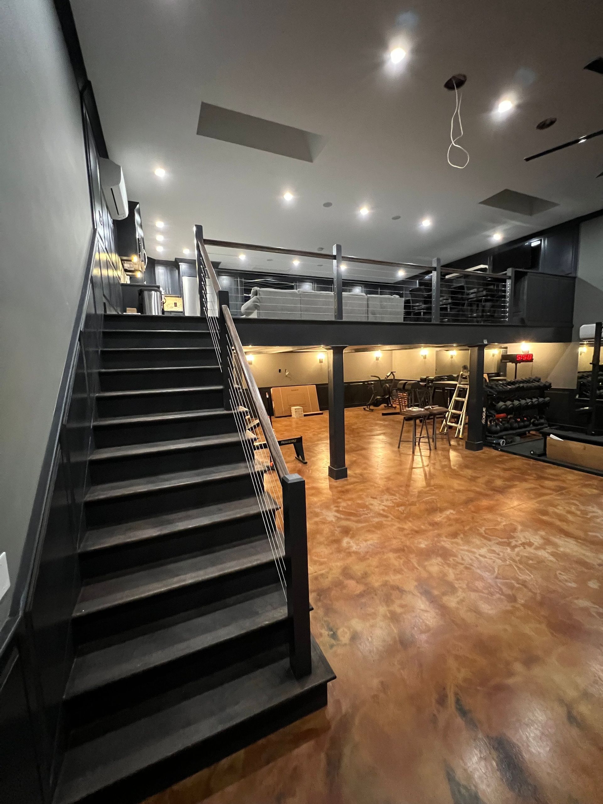 Interior with a dark staircase leading to a loft. The lower level has gym equipment, and the floor is a marbled bronze color.