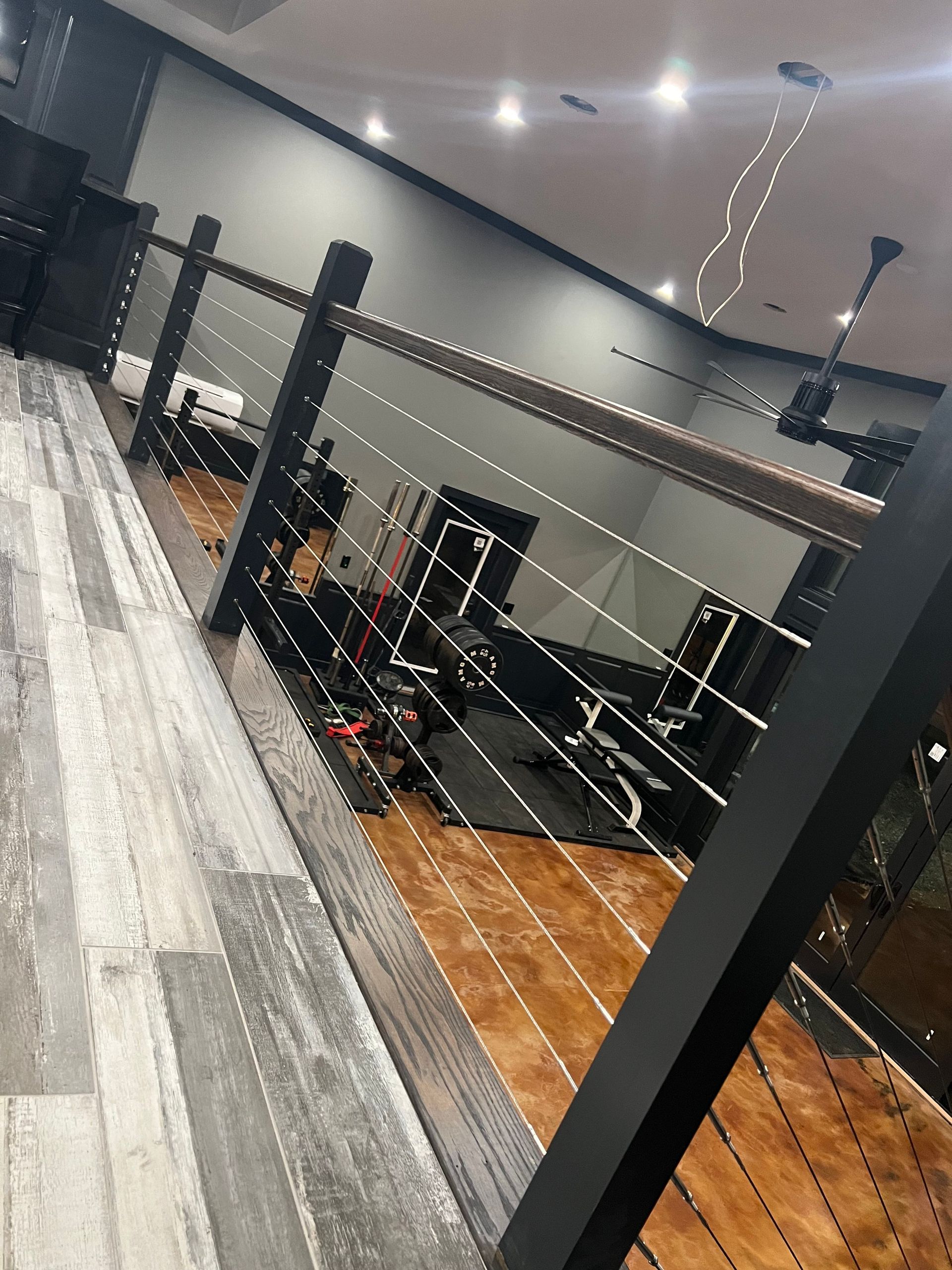 Interior with a wood floor, black railing, and gray walls, looking down on exercise equipment.
