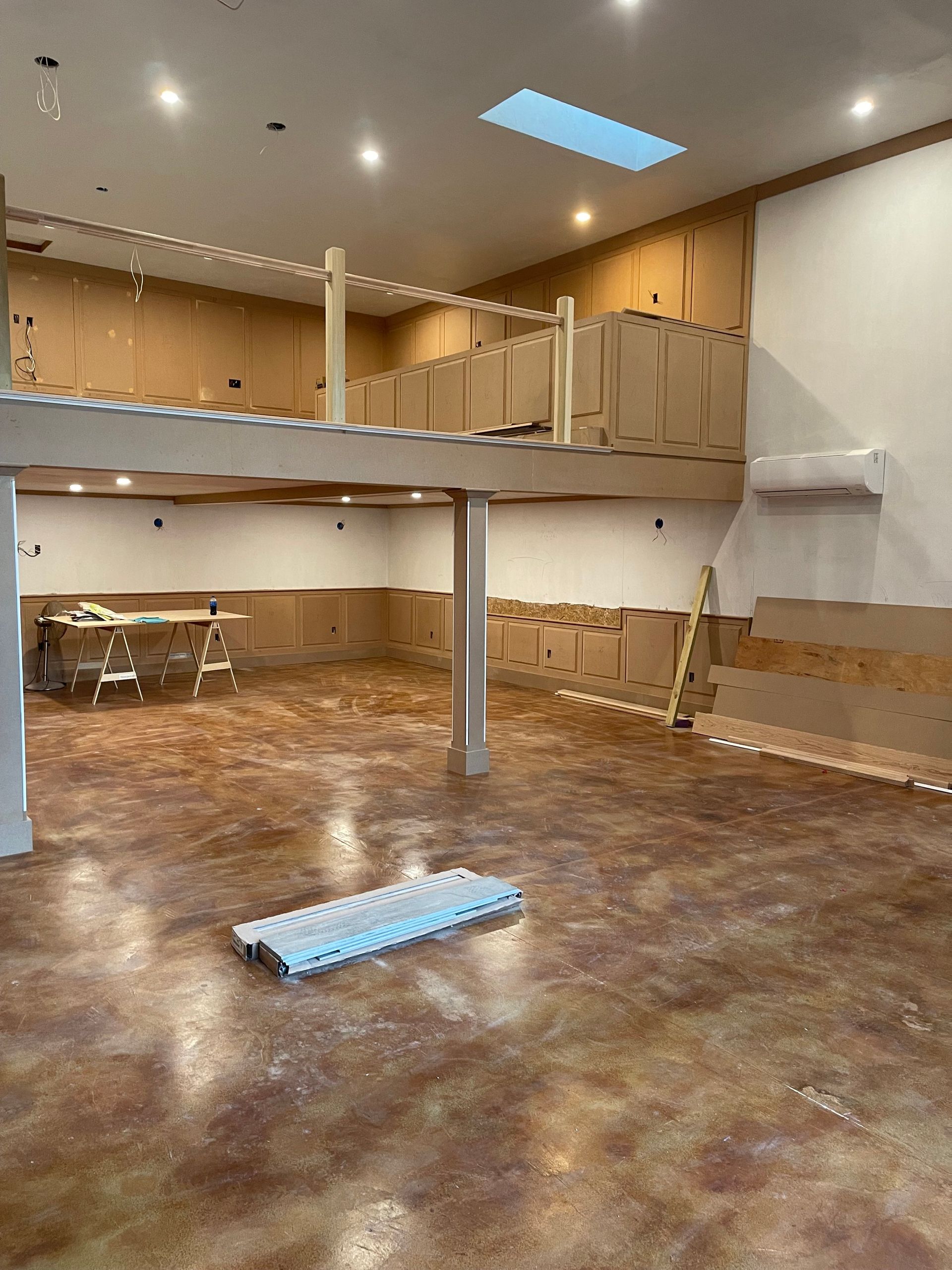 Interior with mezzanine under construction; unfinished wood, tan walls, stained concrete floor, overhead lighting.