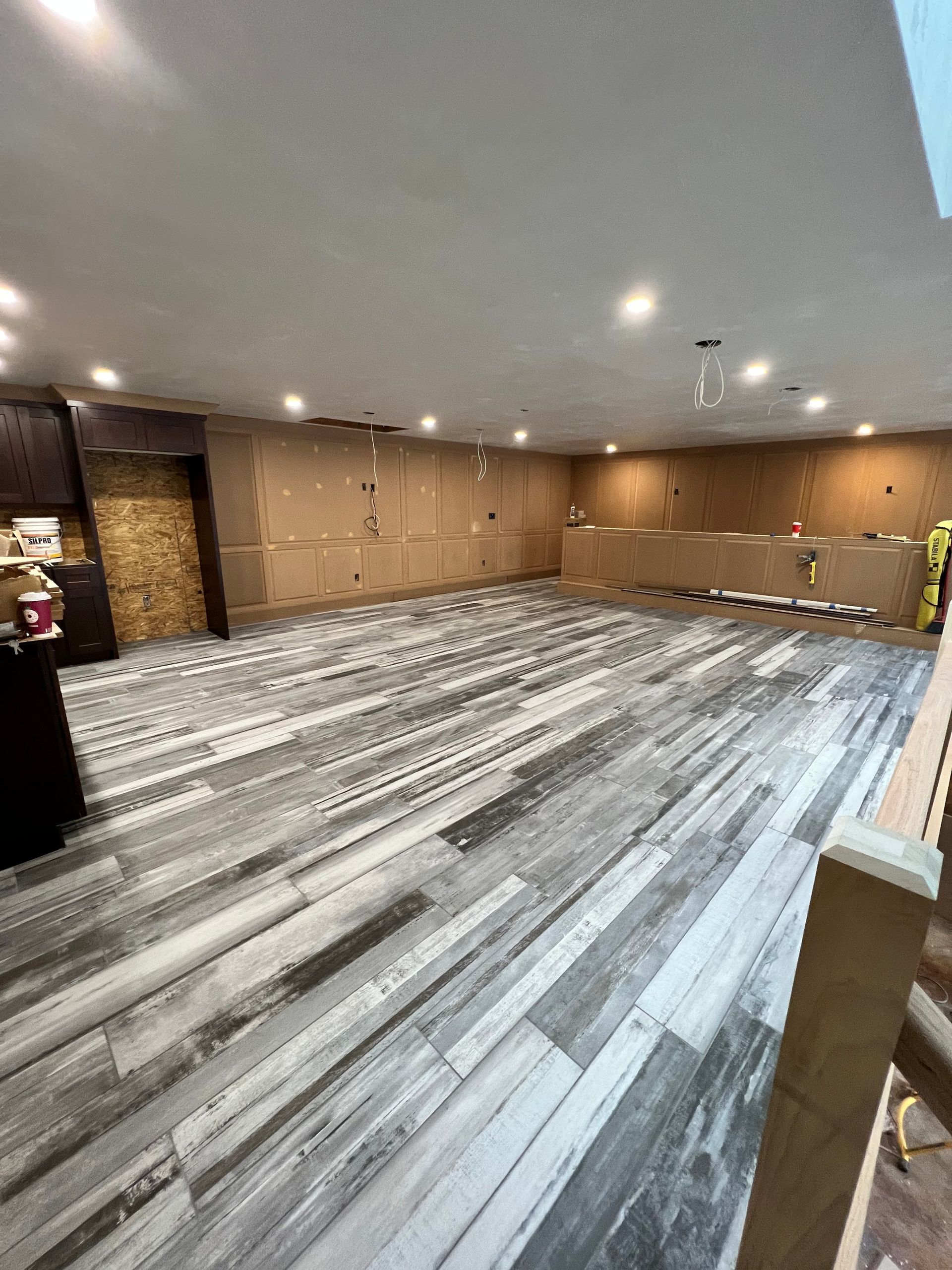 Interior with new wood-look flooring and exposed wall, likely under construction. Overhead recessed lighting.