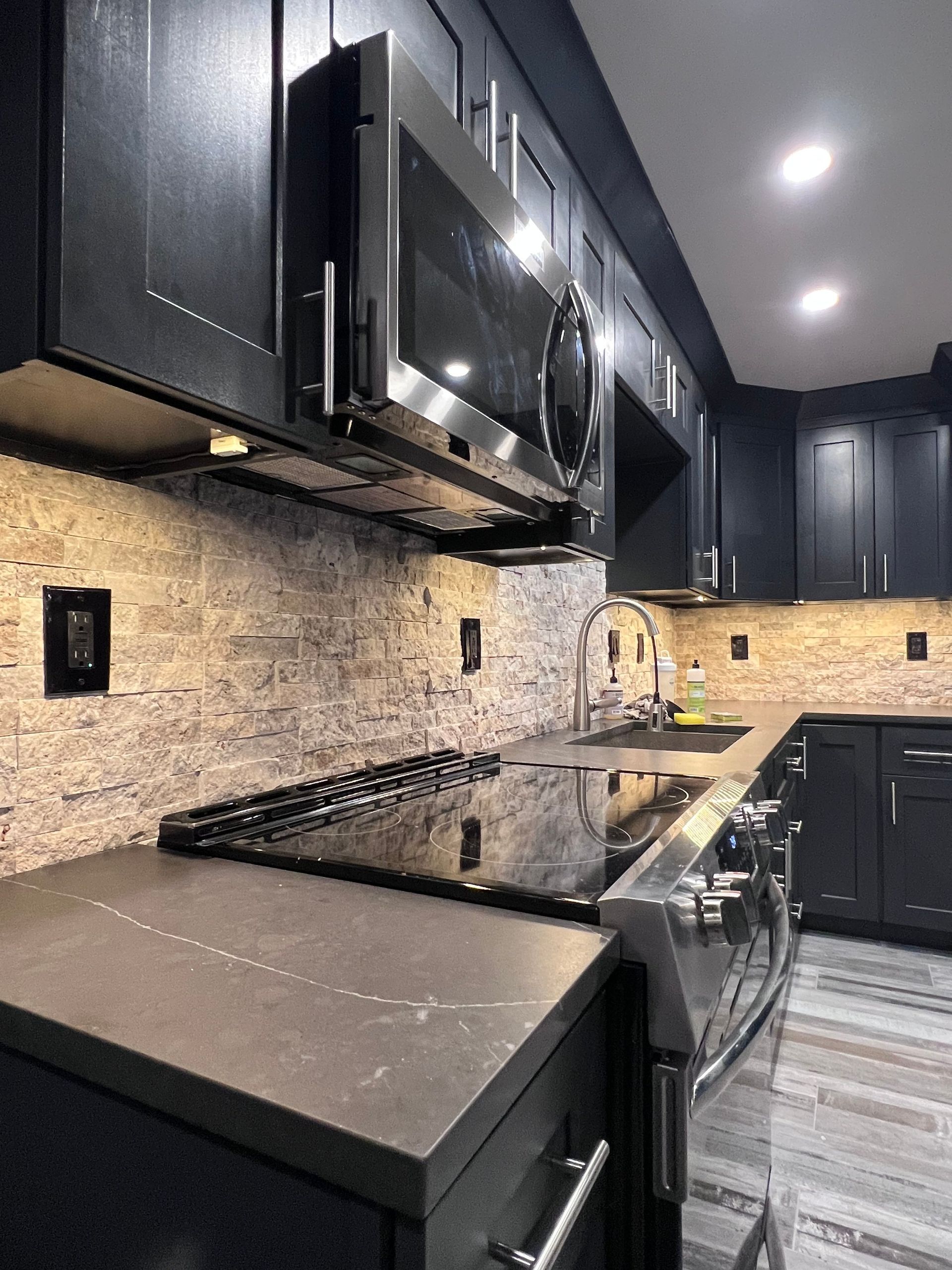 Modern kitchen with black cabinets, stone backsplash, and stainless steel appliances.