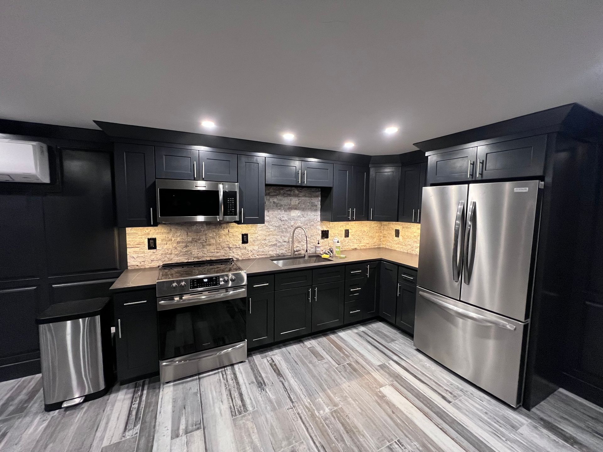 Black kitchen with stainless steel appliances and light wood floors.